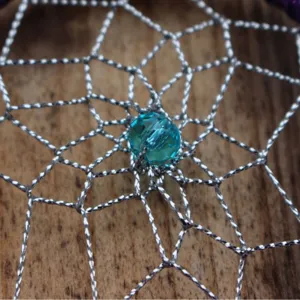 Handcrafted dream catcher center detail with silver woven web and central blue crystal bead.
