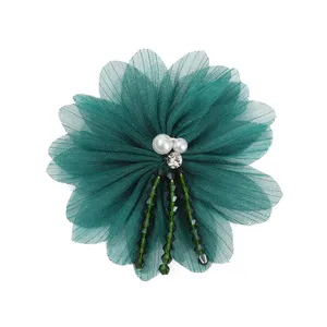 Close-up detail of dark green sheer mesh flower brooch featuring pearls, rhinestones, and beads.