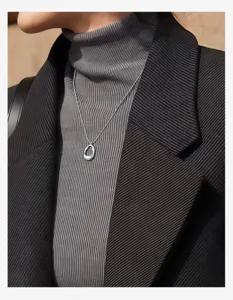 Silver irregular pendant necklace detail shot, elegant minimalist sweater chain accessory.