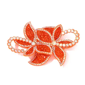 Nahaufnahme der leuchtend orangen Strassblumen-Applikation mit funkelnden Kristall-Details.