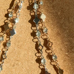 Primo piano dettagliato di catena di gioielli in metallo DIY con ciondoli a trifoglio e strass lucenti.