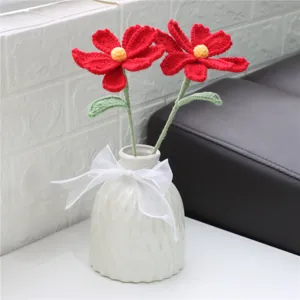 Handmade crochet red cosmos flowers bouquet placed in white ceramic vase for home decor.