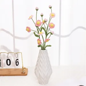 Detailed shot of handmade crochet pink daisy flowers in a white textured ceramic vase.