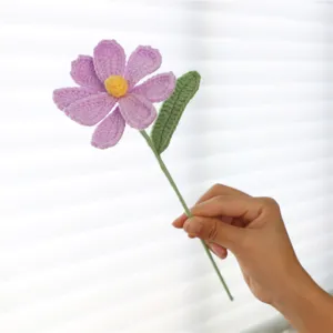 Close-up of handmade crochet cosmos flower detail, showing delicate purple petals and green stem.