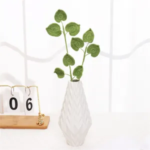Detailed close-up of handmade crochet green plant leaves in a modern white ceramic vase.