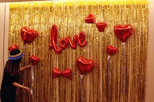 Gold tinsel curtain detail showing metallic foil fringe and romantic red love heart balloons.