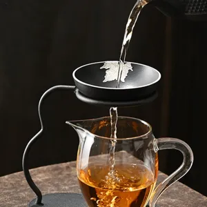 Ensemble tasse de partage en verre et filtre à thé en métal avec décor élégant de feuille.