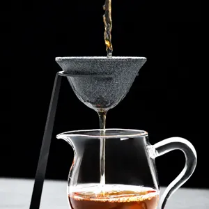 Ensemble de filtre à thé en céramique avec support métallique et tasse en verre transparent.