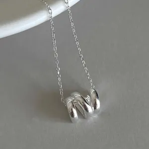 Close-up view of a minimalist silver geometric wave pendant necklace on a neutral background.