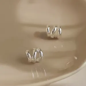 Detailed close-up shot of minimalist multi-strand silver wave earrings on a chic beige dish.