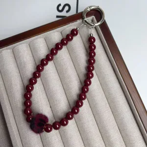 Detailed view of the dark red beaded phone charm strap with fluffy pom pom and metal ring.