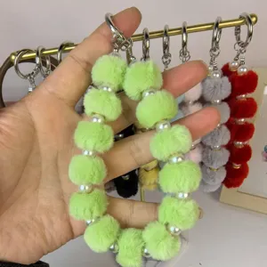 Close-up detail of fluffy lime green pom pom and faux pearl wrist strap keychain charm.