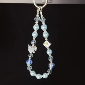 Close-up detail of blue crystal pearl beaded phone charm wrist strap with bow and metal pendant.