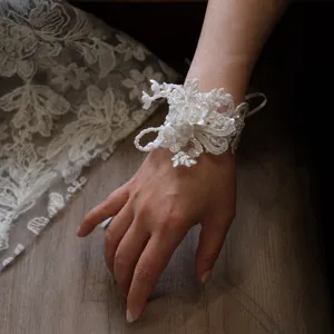 Detailed close-up of white lace wrist flower with pearls for wedding bridal decoration.