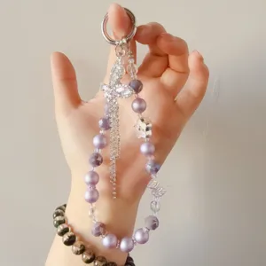Close-up detail of purple beaded phone charm with sparkling rhinestone bow pendant and crystals.