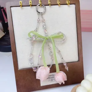 Close-up detail of beaded cell phone charm with pink tulip pendants and green ribbon bow.