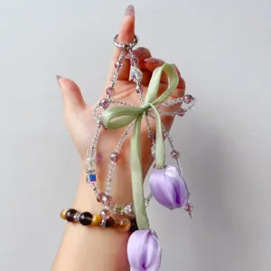 Closeup of handmade beaded phone charm featuring purple fabric tulips and green ribbon bow.