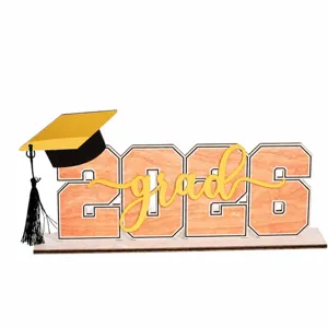 Primo piano dettaglio del centro tavola in legno di laurea 2026 con lettera e cappello.