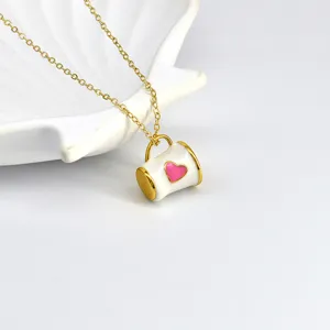 Gros plan d'un collier pendentif tasse émaillée doré avec un détail de cœur rose.