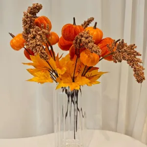 Artificial velvet pumpkin branch with autumn maple leaves and berries in glass vase.