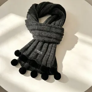 Close-up detail view of dark grey knitted pom pom scarf, cozy and warm winter accessory.