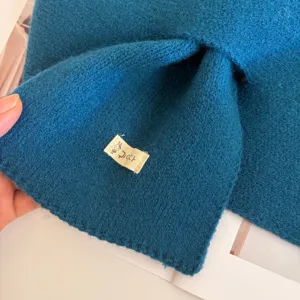 Close-up detail of dark blue knitted cross scarf, showing soft wool texture and cute tag.