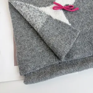 Close-up detail of grey knitted winter scarf with cute pink bow and soft wool texture.