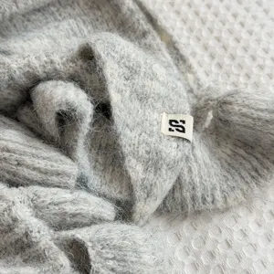 Close-up view of soft fuzzy knit shawl detail, showing cozy texture and branded tag.