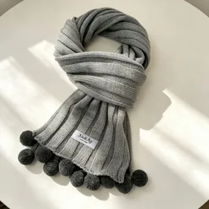 Grey knit winter scarf detail with cute pom pom accents, cozy warm fabric texture.