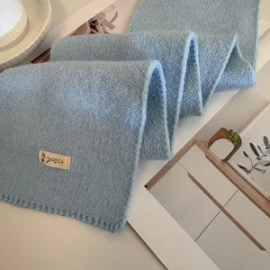 Detailed close-up of the soft light blue knitted scarf, highlighting fine texture and fabric label.