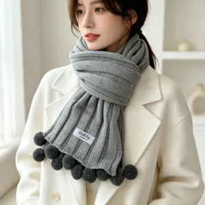 Grey knitted scarf with cute pom-pom details, cozy winter accessory for women close-up view.