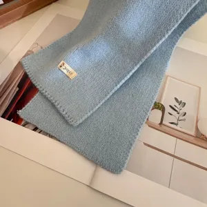 Detailed view of soft light blue knitted scarf with cute woven label, cozy winter accessory.
