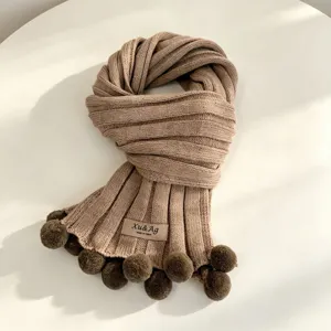 Knit winter scarf detail showing soft textured wool fabric, warm ribbed design and cute pom poms.