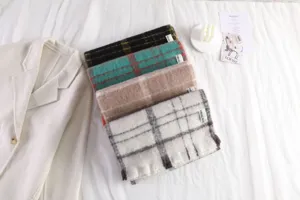 Detailed shot of cozy mohair plaid scarves in various colors displayed neatly on white bedding.