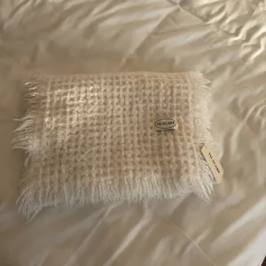 Detailed close-up view of a cozy cream knitted winter scarf featuring fringe and a chic brand label.