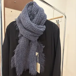 Detailed view of the cozy greyish blue knitted wool scarf with fringe edges in showroom.