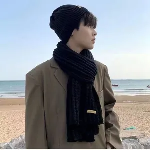 Detail shot of a black knitted beanie and cozy winter scarf, outdoors lifestyle beach view.