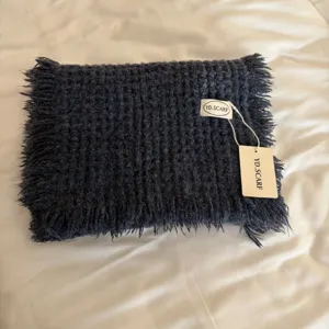 Close-up of a cozy dark grey knitted scarf featuring handmade fringe and brand label.