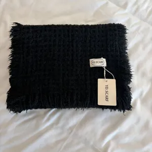 Black knitted scarf detail showing soft textured wool fabric and brand label tag.