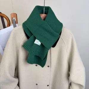 Dettaglio della sciarpa in maglia verde scuro su cappotto beige, morbida ideale per inverno.