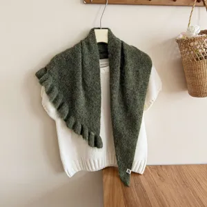 Charming dark green ruffled knit shawl detail, cozy cape style overlaying white top.