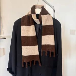 Nahaufnahme des braun-beigen gestreiften Strickschals an Mantel, gemütliches Winteraccessoire.