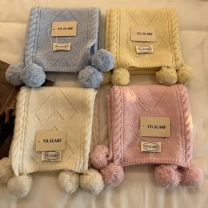 Detailed view of soft knitted winter scarves with cute pom-pom ends in pastel colors.