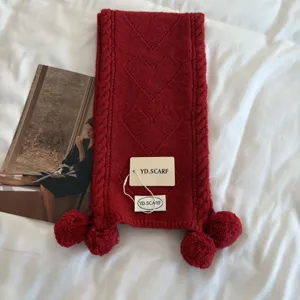 Close-up detail of cozy red knitted scarf with cute pom-poms and heart texture pattern.