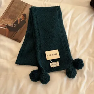 Dark green knitted scarf detail view, featuring cozy pom-pom accents and soft texture.