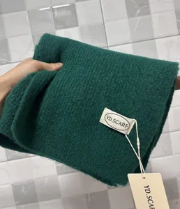 Detailed shot of dark green knitted winter scarf, soft wool texture with brand label.