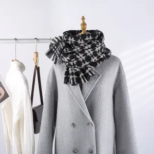 Detailed close-up view of a stylish black and white grid scarf displayed in a cozy winter scene.