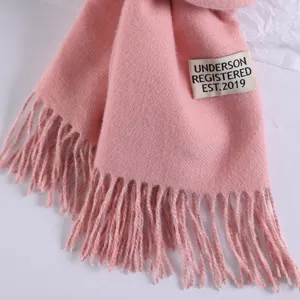 Close-up detail of a soft pink winter scarf featuring chic fringe edges and a stitched label.