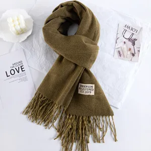 Detail view of thick imitation cashmere winter scarf with tassels and tag in olive green.