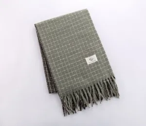 Detailed view of green plaid winter scarf featuring decorative fringes and soft textured fabric.